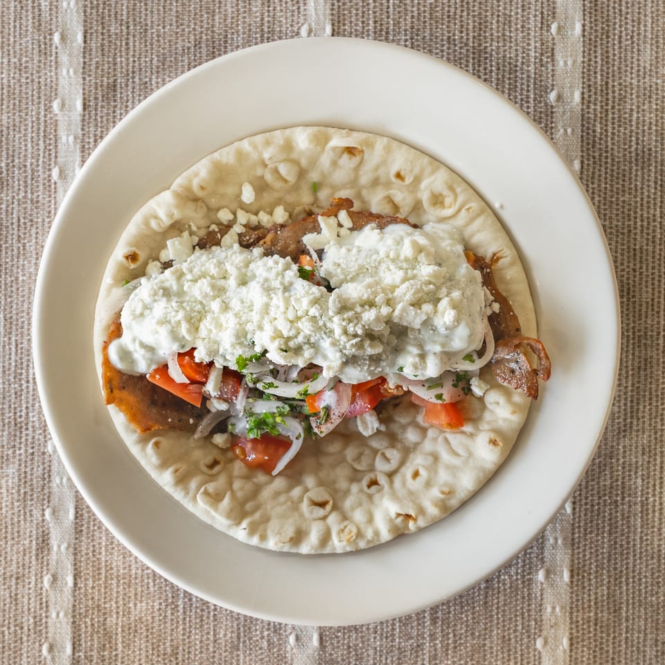 Overhead view of a gyro on pita bread, topped with meat, tomatoes, onions, and feta cheese.