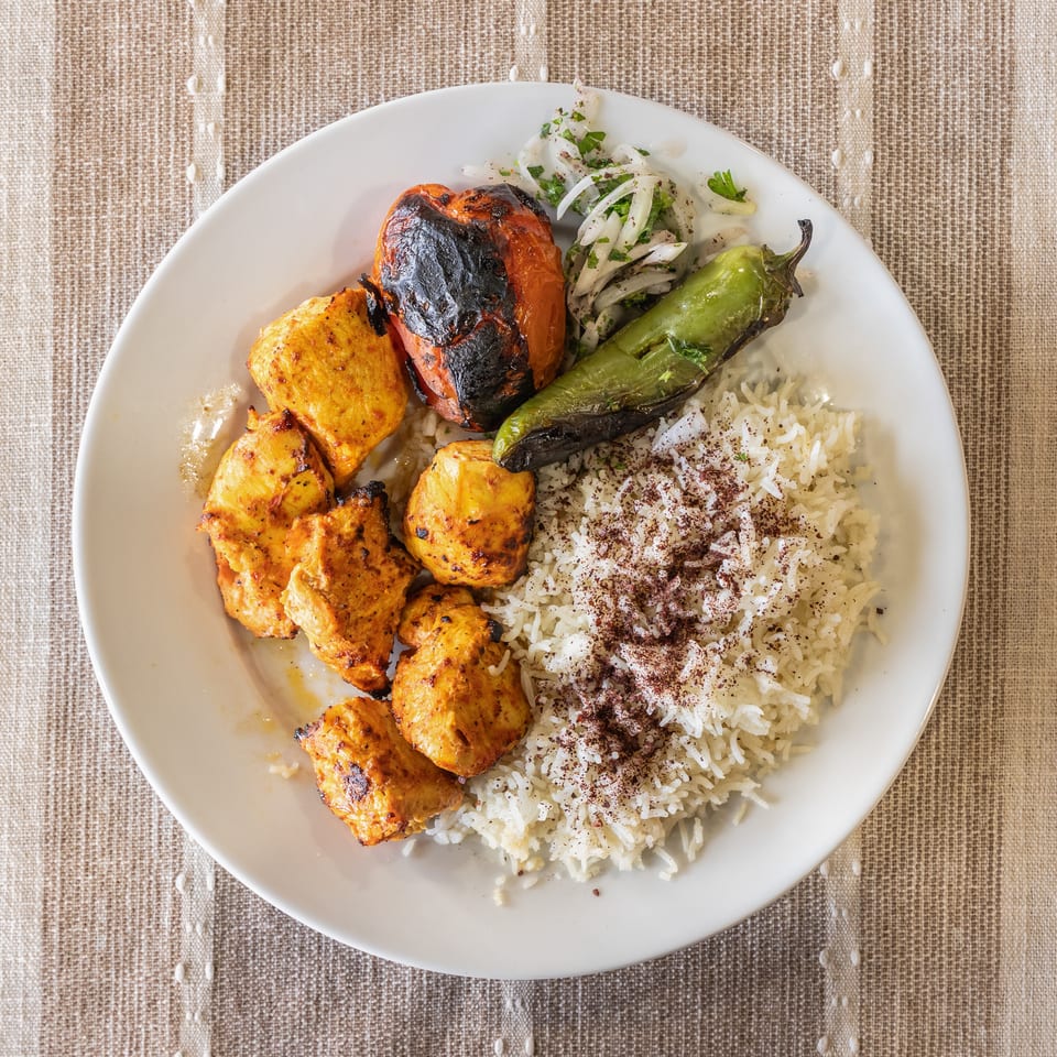 Chicken shish tawook with rice, grilled tomato, pepper, and onion salad on a white plate.
